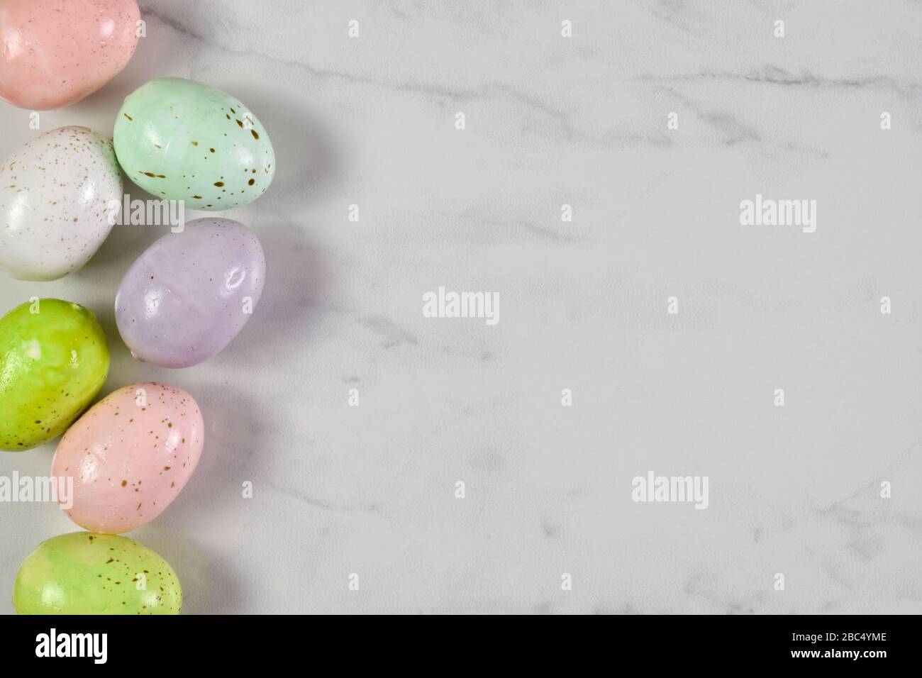 Colorful speckled Easter eggs resting joyously on a white marble background. Stock Photo