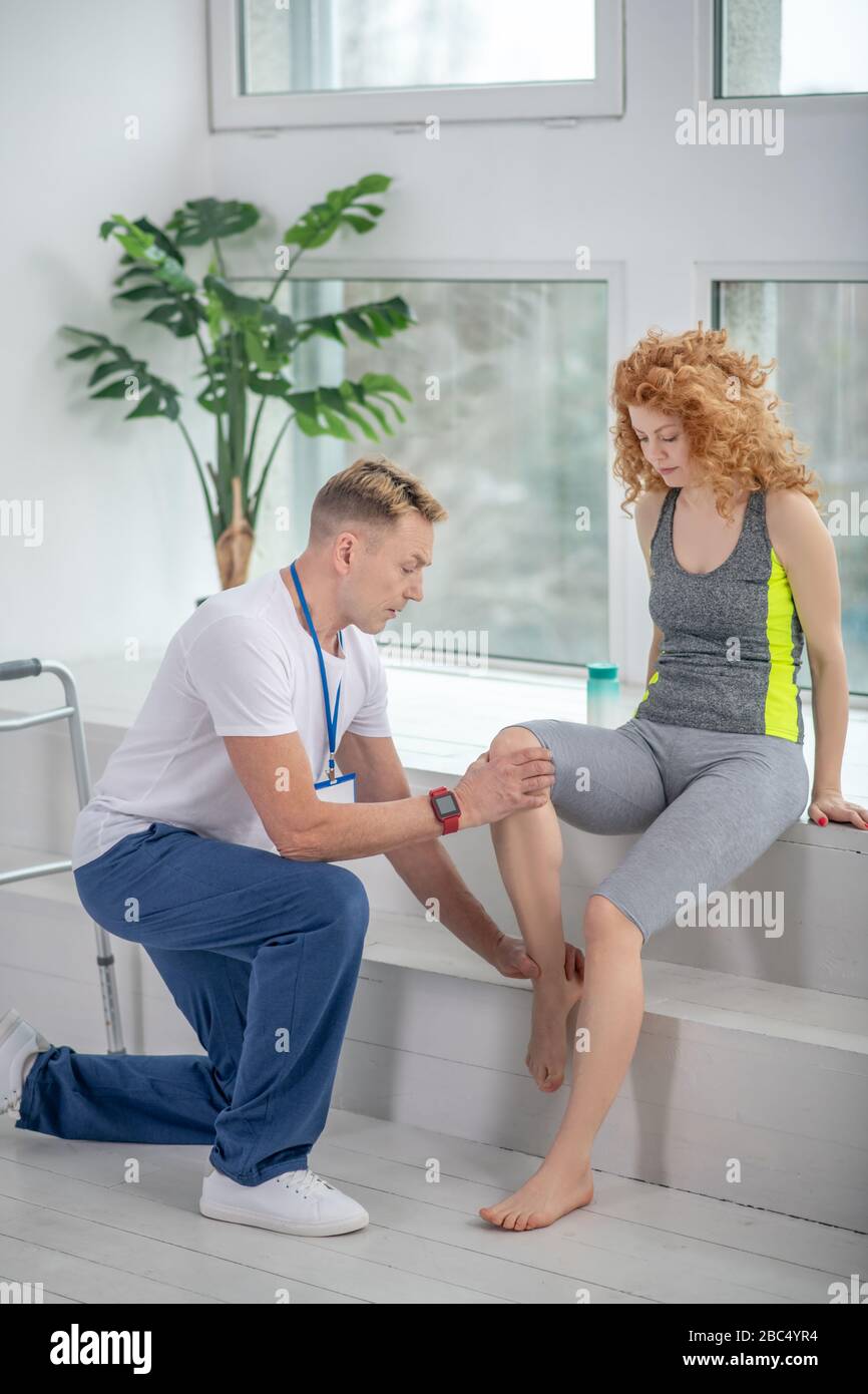 Male physiotherapist kneeling on one knee, examining painful knee of