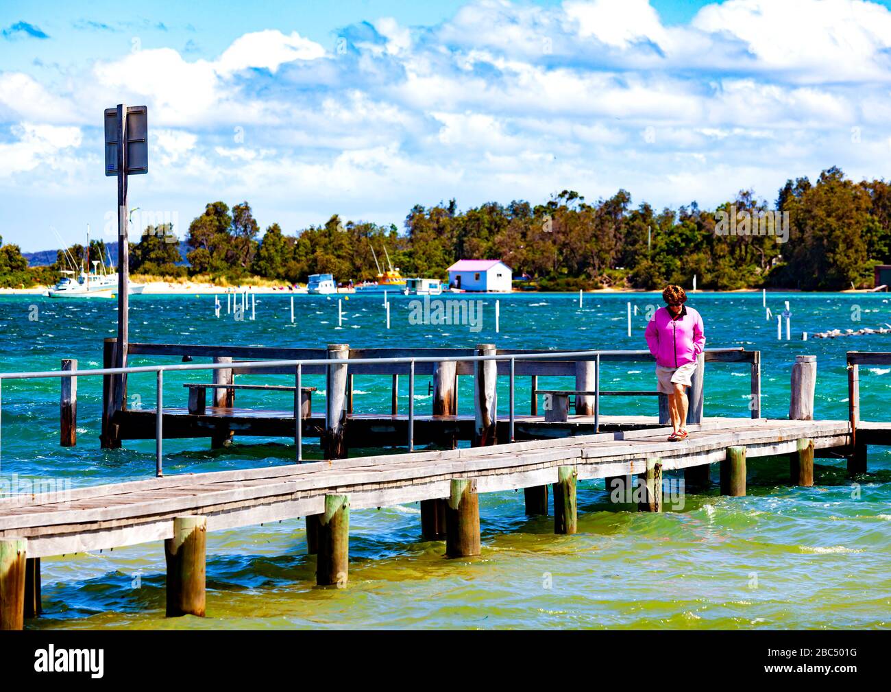 Thoughtful woman in pink top walking along boardwalk in Merimbula on New South Wales south coast Stock Photo