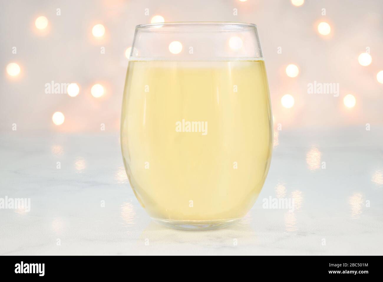 No Stem Wineglass mockup featuring a stemless wine glass filled with white wine. White lights glow romantically in the background. Stock Photo