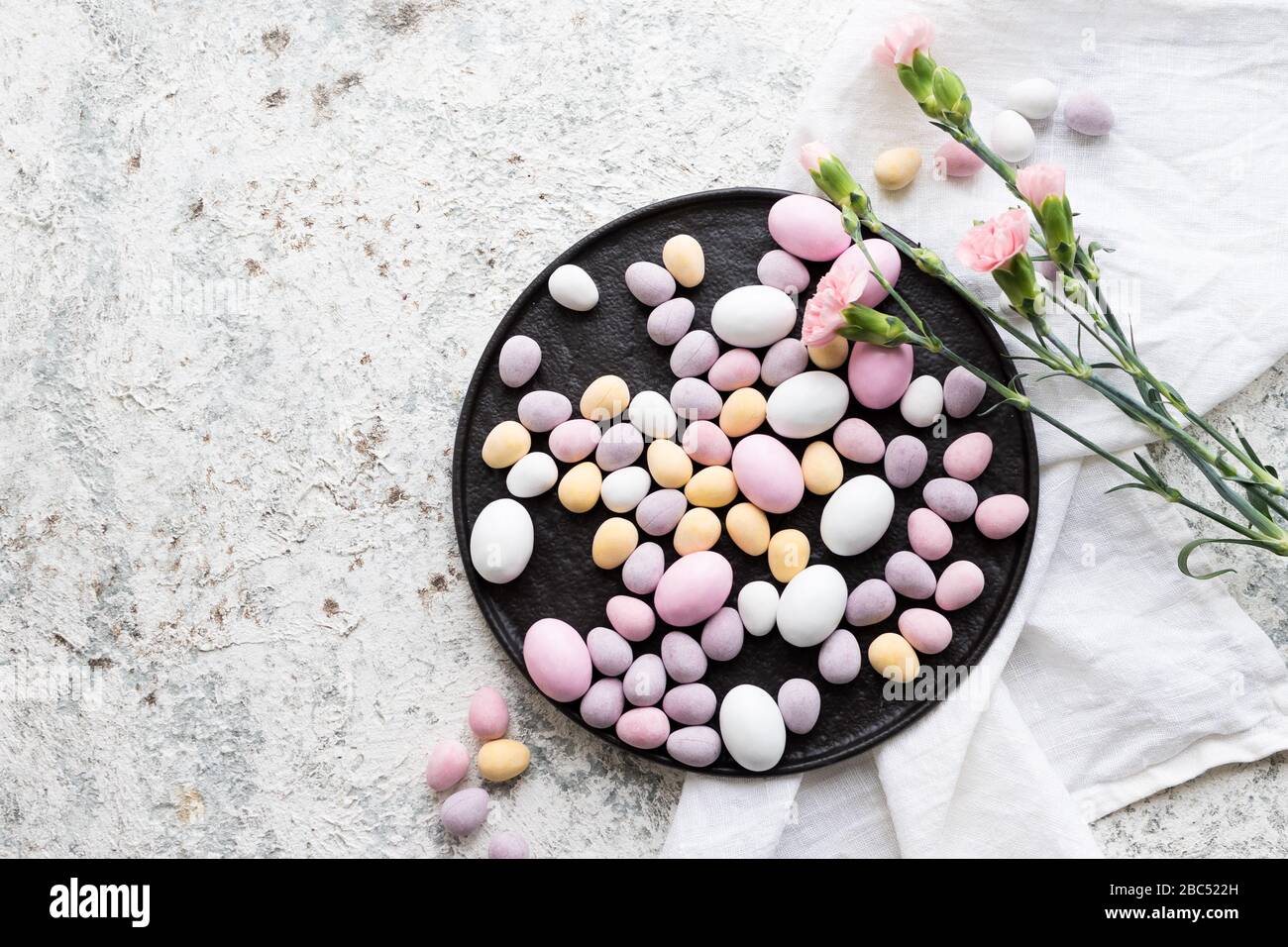 Easter composition with mini chocolate eggs in pastel colors and pink flowers on grey concrete background. Happy Easter Holidays. Top view. Copy space Stock Photo