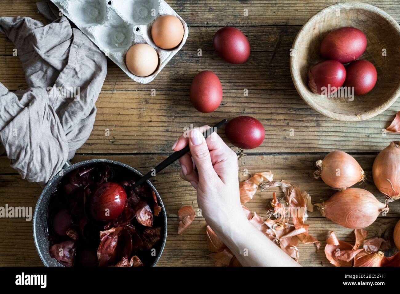 Woman making dyed Easter eggs painted with natural dye onion on wooden background. Process of dyeing eggs with natural paints for Easter. Natural ecol Stock Photo