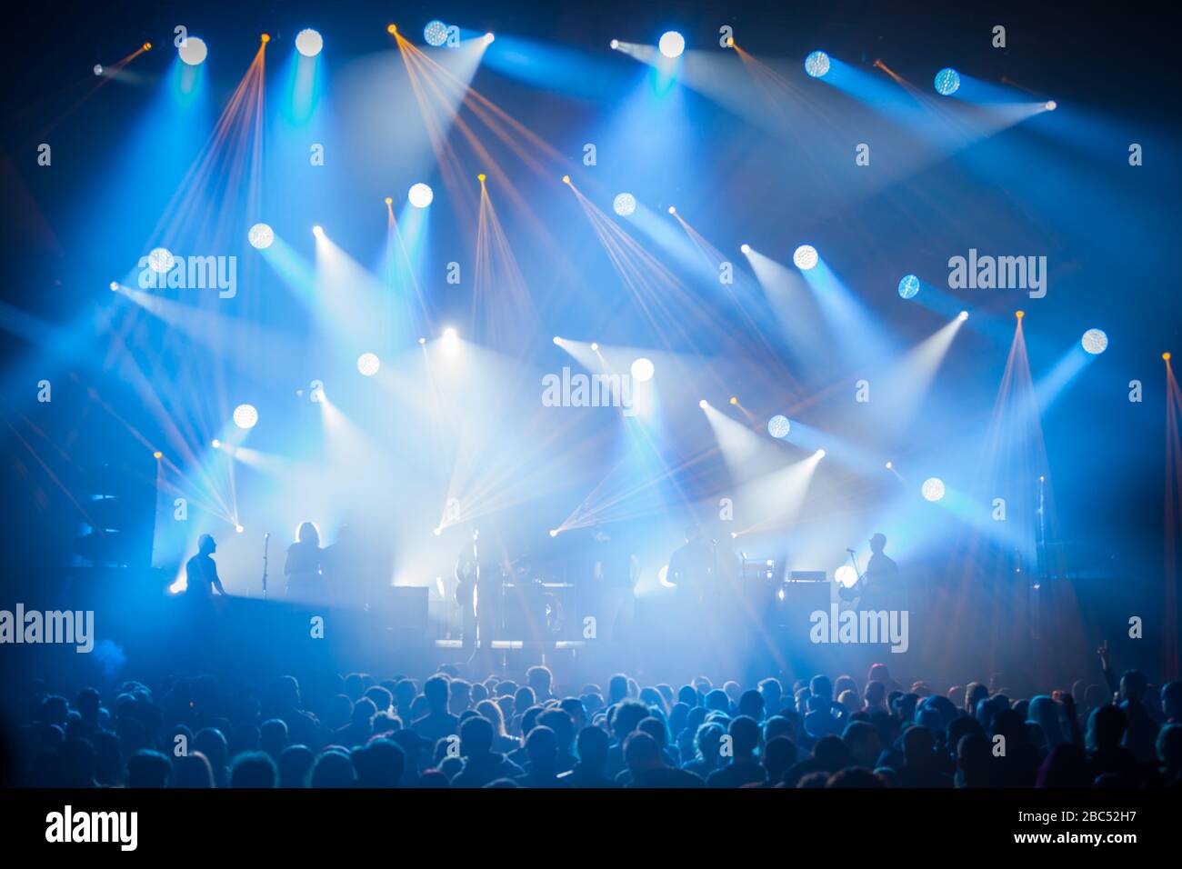 Stage lights on concert. Lighting equipment with multi-colored beams. Silhouettes of people and musicians in big concert stage. Stock Photo
