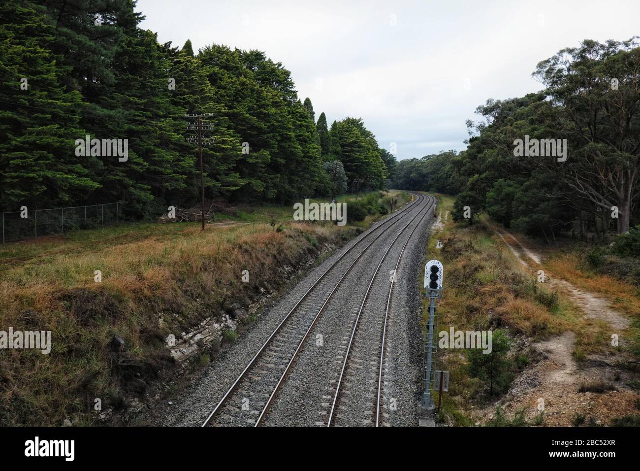 Landscape image of the Southern Highlands Train line, dirt service road and conifer trees on an overcast morning, Mittagong NSW Stock Photo