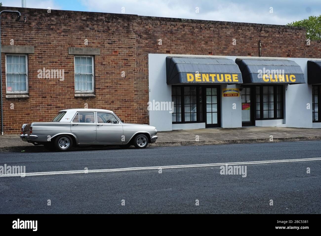 Vintage two tone silver & white EH Holden car parked on the street, a brick wall, & sign Denture Clinic, in Mittagong, Southern Highlands, Australia Stock Photo