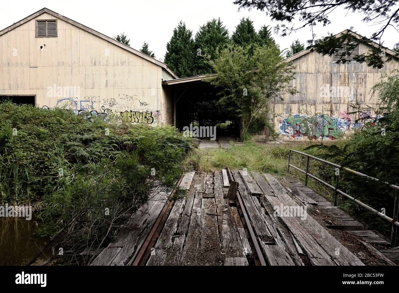 Rotten timber plank bridge over the Nattai River at The Maltings, corrugated iron warehouses on the derelict industrial site Mittagong, NSW Stock Photo