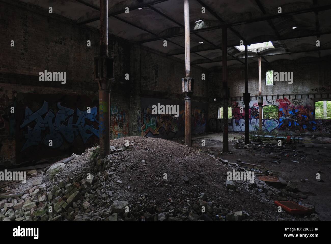 Ground floor interior with cast iron columns, dirt pile, window light & graffiti walls;  The Maltings abandoned industrial site, Mittagong NSW Stock Photo