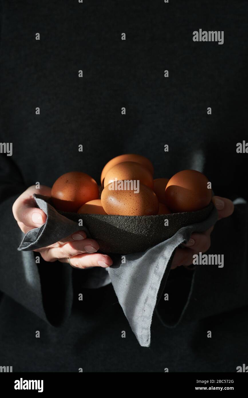 Unusual Easter on a dark background. A bowl of brown eggs with hands. Stock Photo