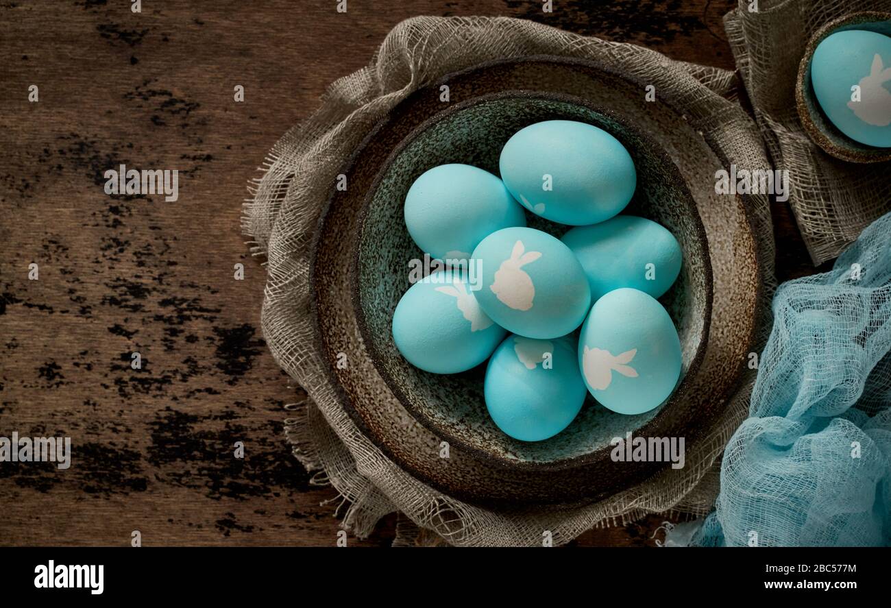 Unusual Easter on dark old background. Ceramic brown bowl with blue eggs with rabbit. Stock Photo