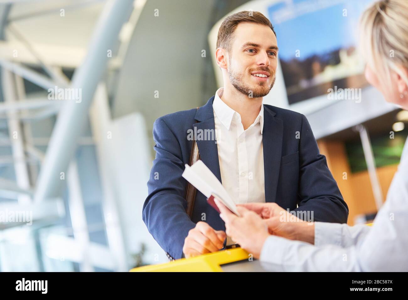 Service agent at the check-in counter in the airport checks boarding pass of a businessman Stock Photo