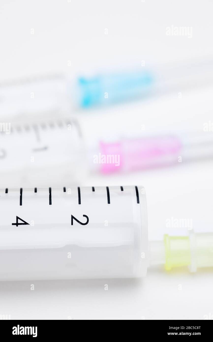 Three syringes in different sizes and colors on white background used as medical equipment - selective focus Stock Photo