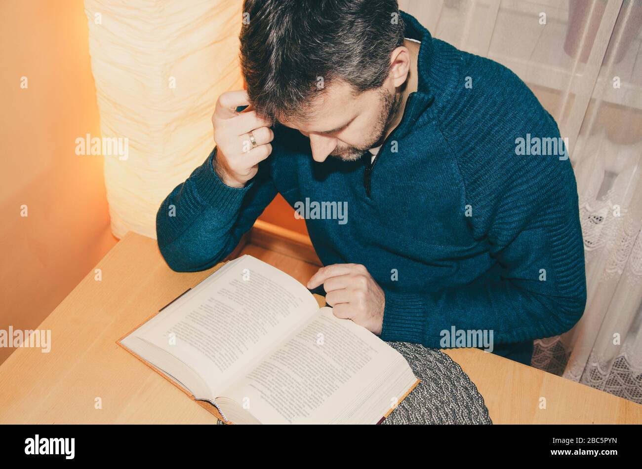 A mature man reading a book at the wooden table at home. Stay at home order Stock Photo