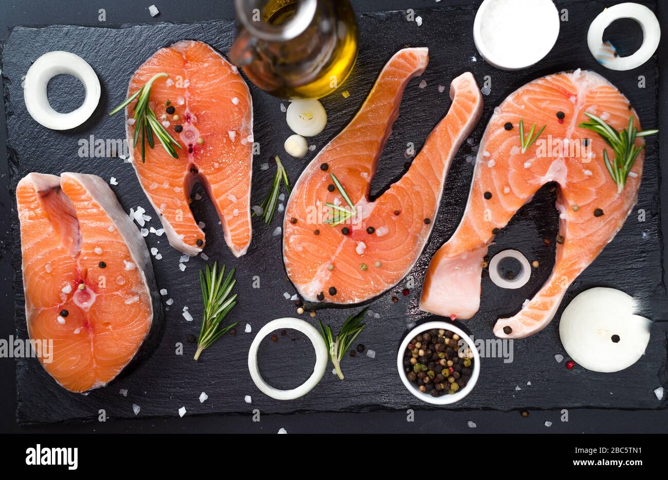 raw salmon steak on a dark stone background with onions, rosemary