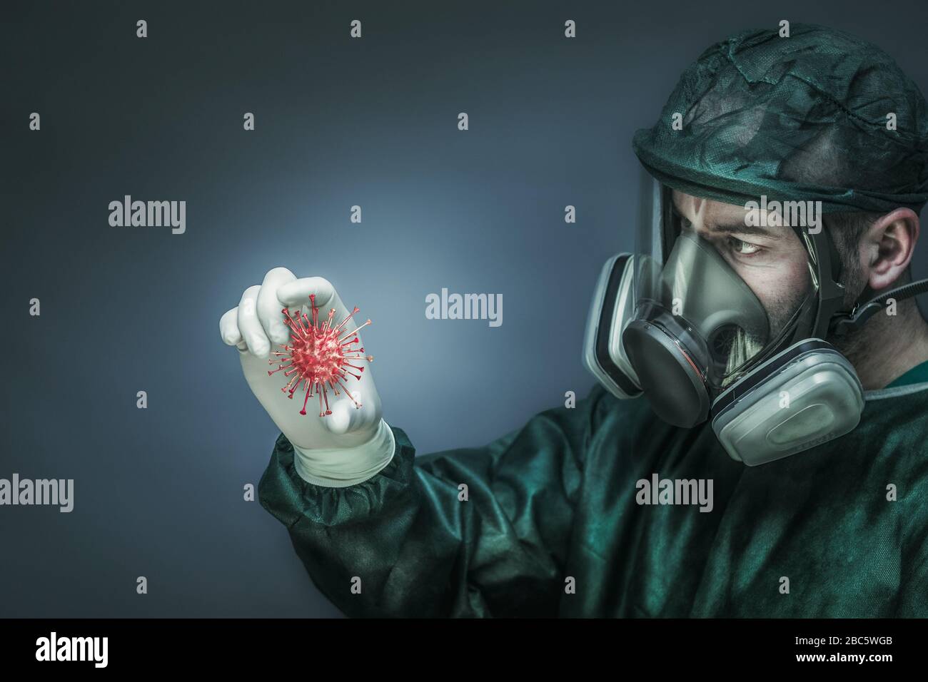 doctor wearing protective clothes and a large mask with filters looks at the virtual coronavirus model between his fingers. concept of health and prev Stock Photo