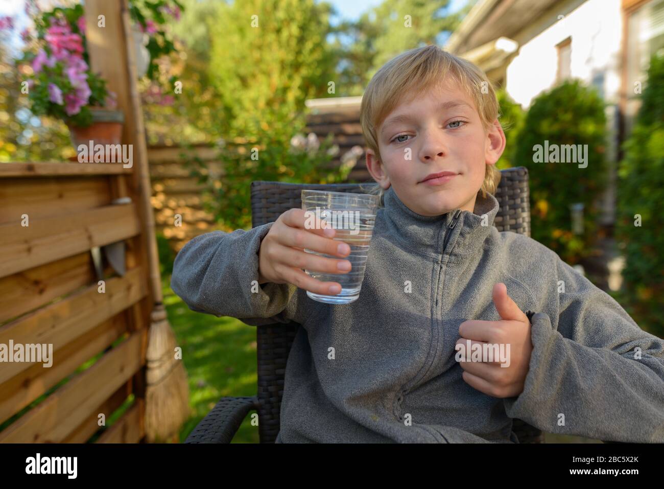 Young handsome boy with glass of water giving thumbs up in the backyard Stock Photo