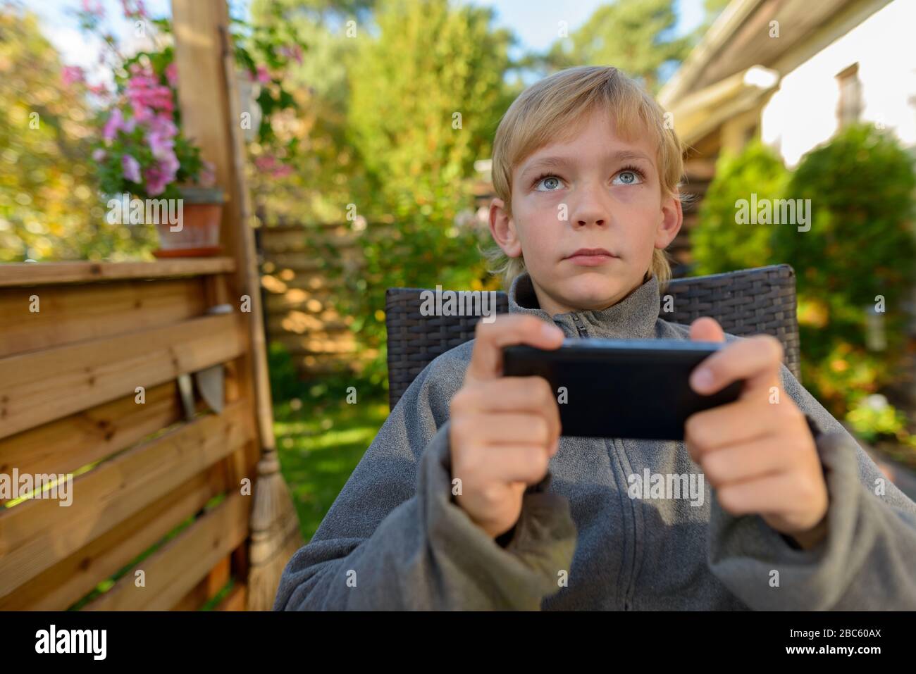 Young handsome boy thinking while using phone in the backyard Stock Photo
