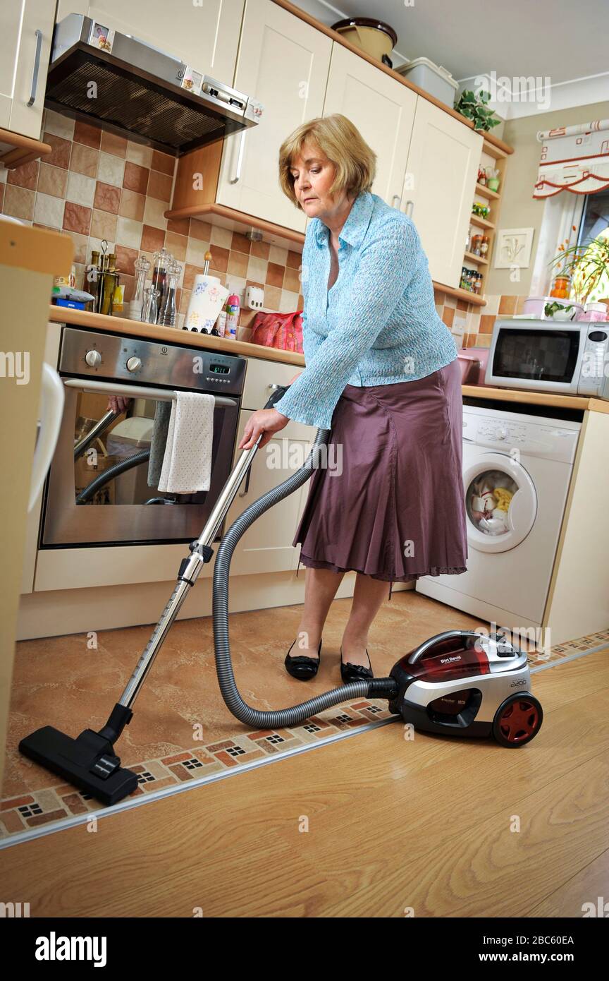 Older woman vacuum cleaning in her kitchen at home. Excessive cleaning  can be a sign of OCD, Obsessive Compulsive disorder. Stock Photo