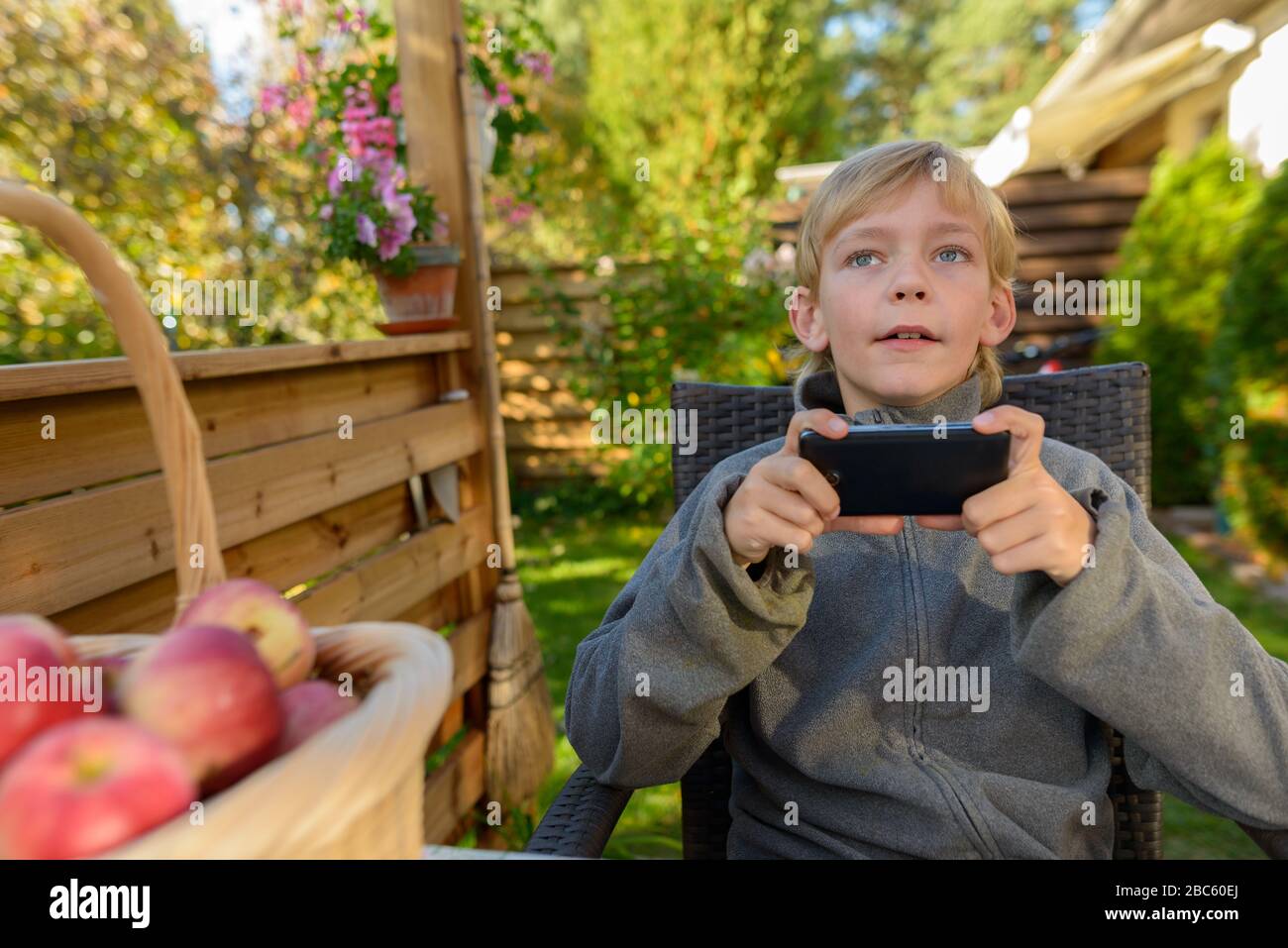 Young handsome boy thinking while using phone in the backyard Stock Photo