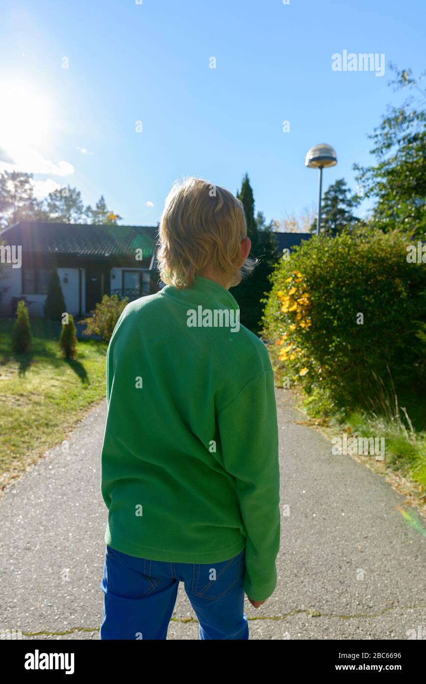 Rear view of young boy with blond hair in the front yard Stock Photo