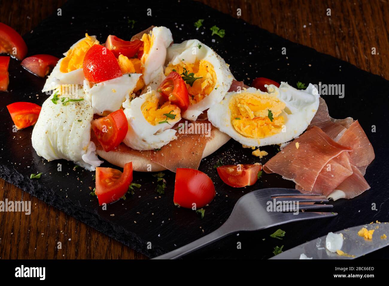 Eating boiled egg with parma ham and cherry tomatoes Stock Photo