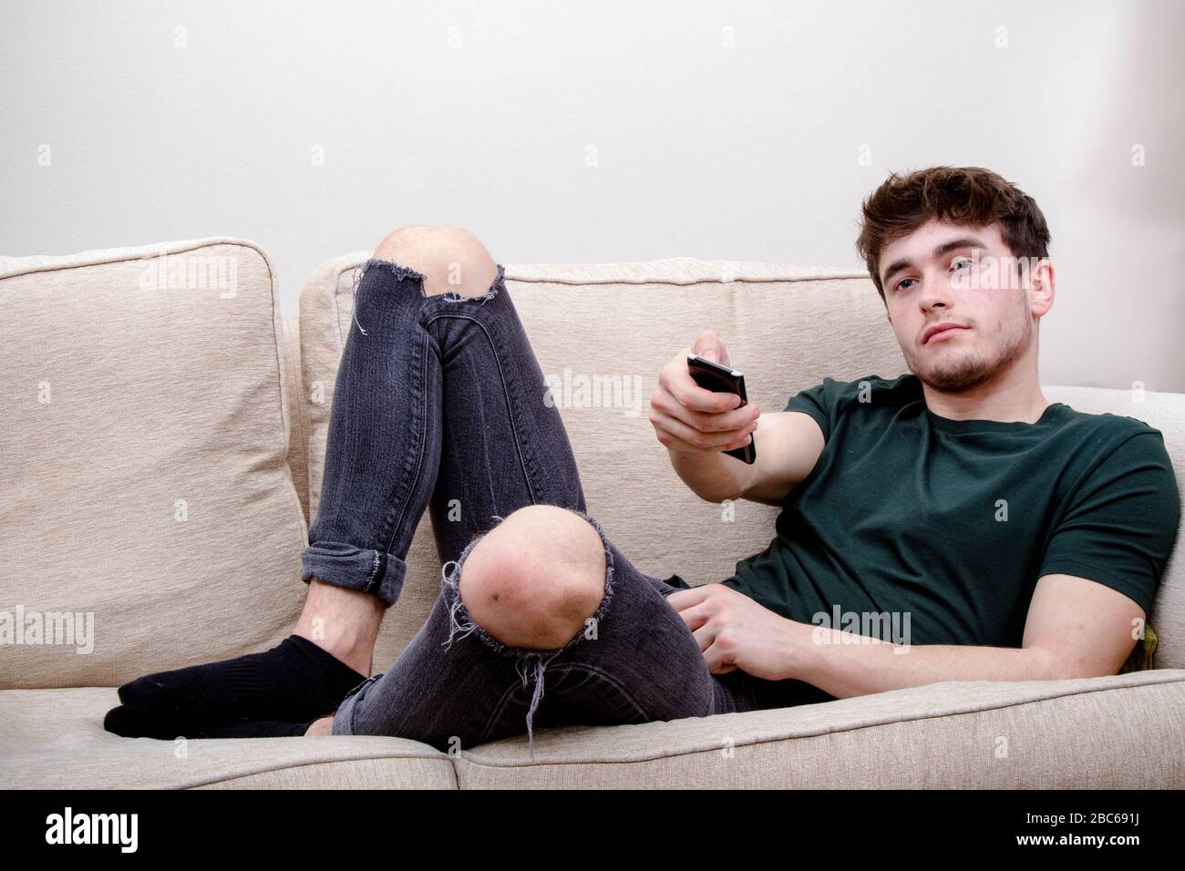 Man Using Remote Control A young adult man using a remote control while on a sofa Stock Photo ...