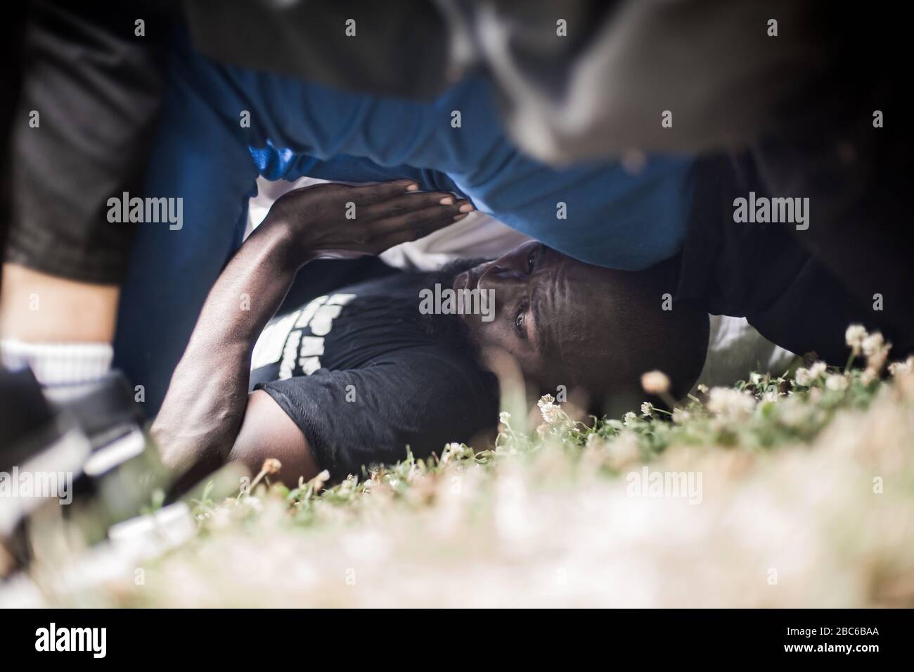 A man crawls across the ground on his back and sneaks under a large group of people, on military type endurance training boot camp, outdoor in nature Stock Photo