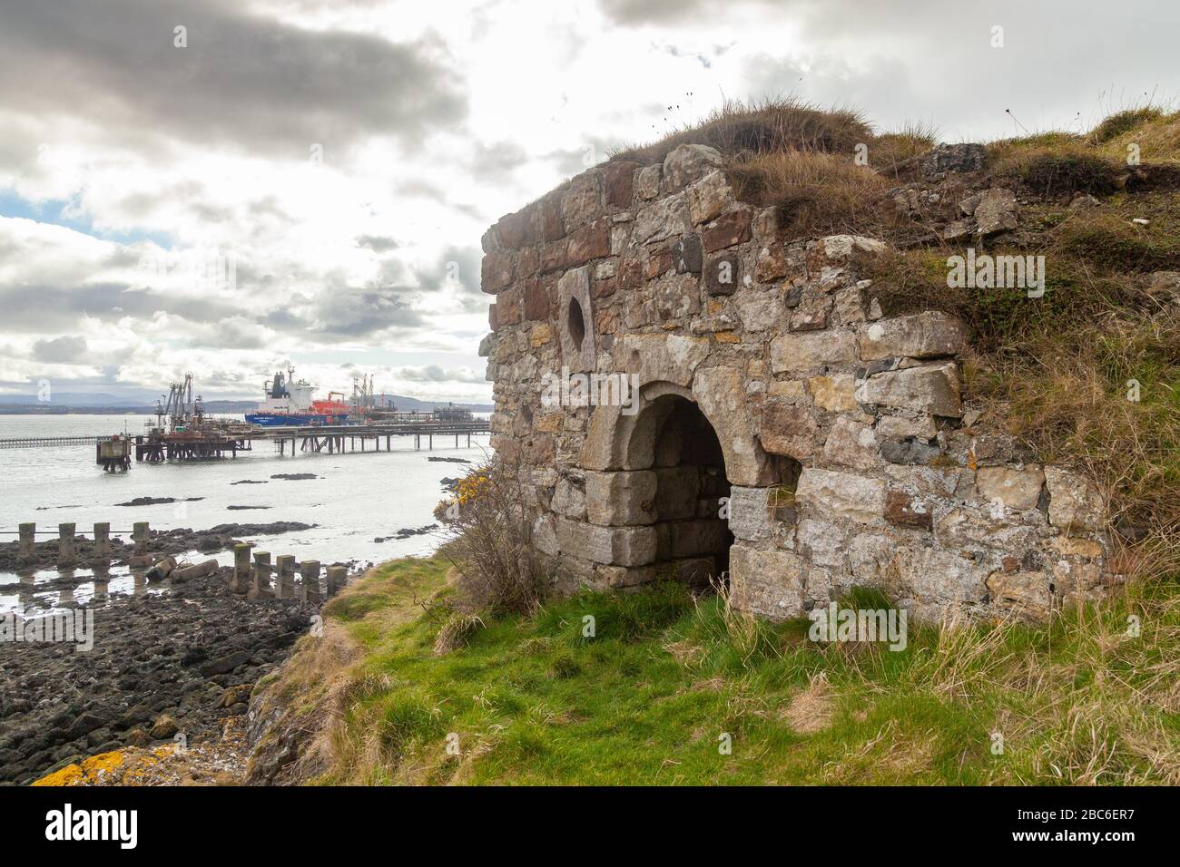 Monk's Cave with Braefoot Oil Terminal in the background, Dalgety Bay, Fife, Scotland. Stock Photo