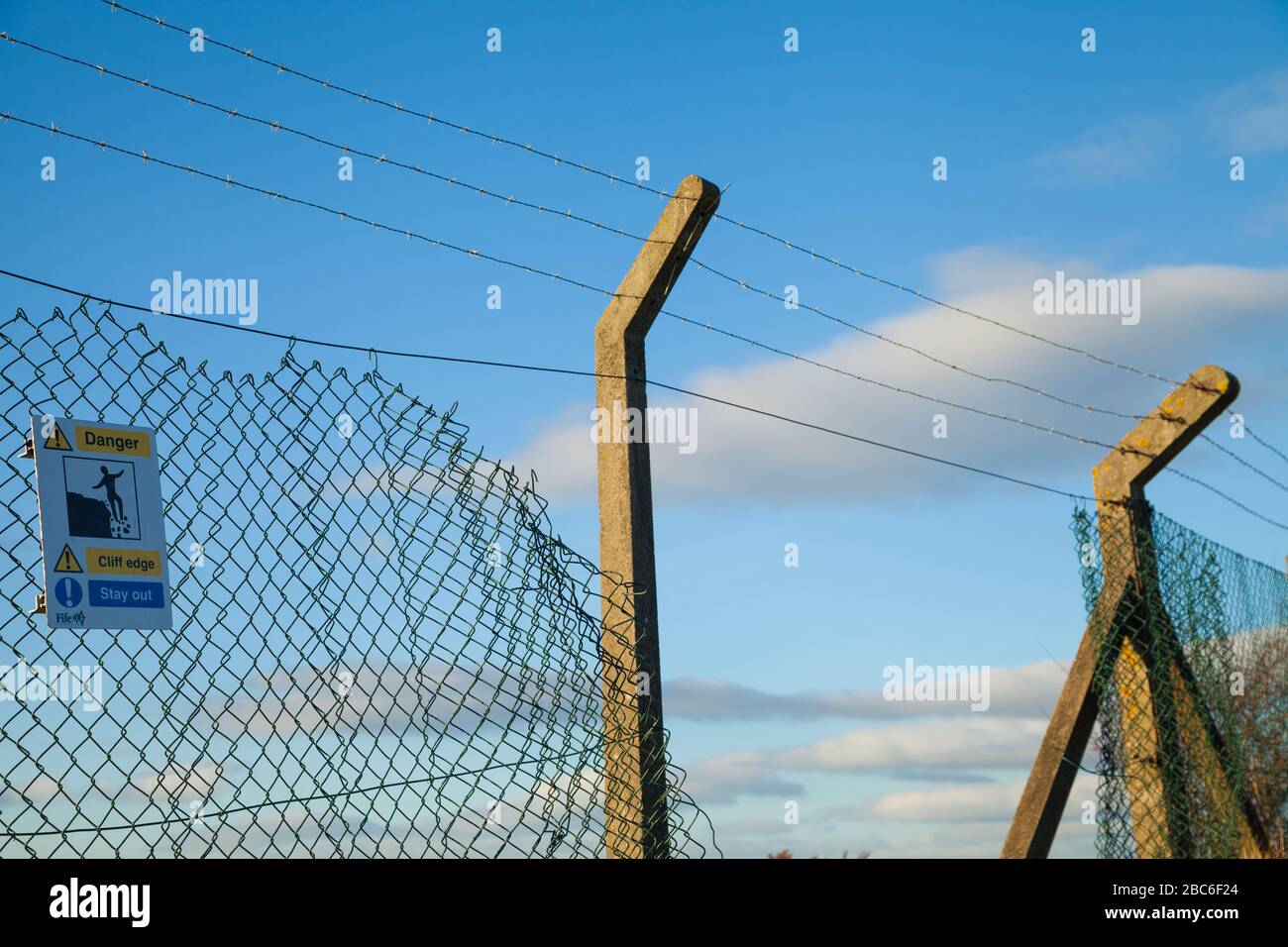 A  broken chainlink fence protecting a steep edge. Stock Photo