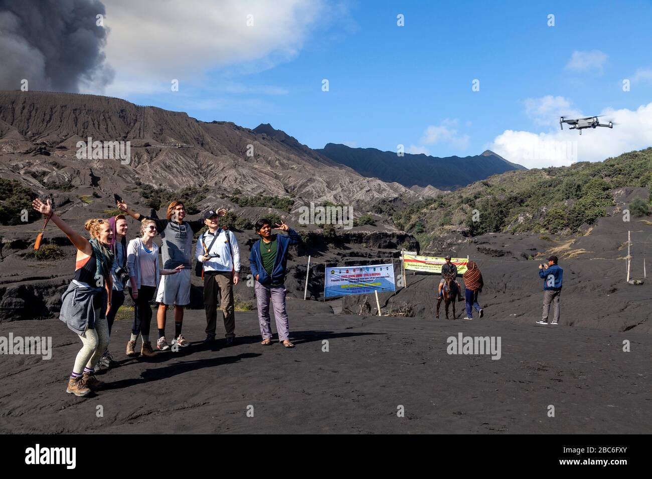 Tourists Pose For A Drone Selfie On The Sea Of Sand, In The Backround Is An Erupting Mount Bromo, Bromo Tengger Semeru National Park, Java, Indonesia Stock Photo