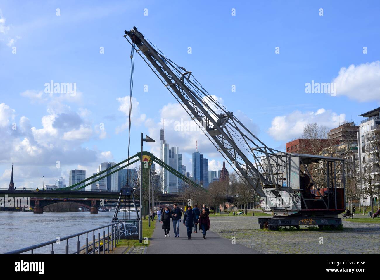 Frankfurt Main, Germany 03-14-2020 people walking on the river main nea the Weseler Werft passing an historic crane Stock Photo