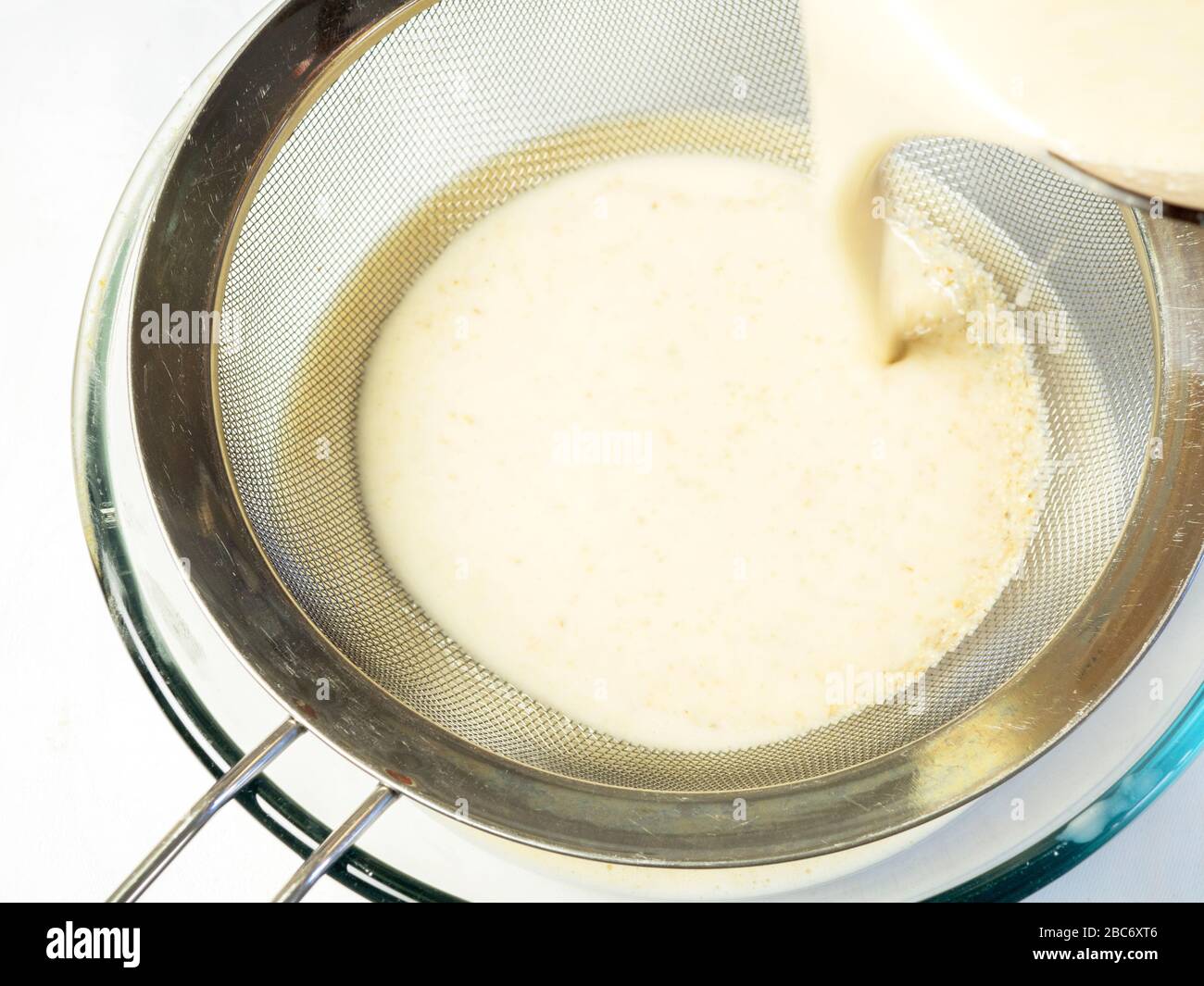 Straining blended dairy alternative oat cream through a steel sieve into a glass bowl on a white tablecloth Stock Photo