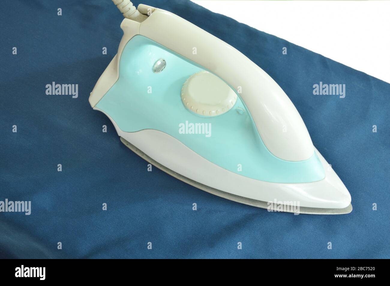 blue automatic electric iron pressing cloth on ironing board Stock