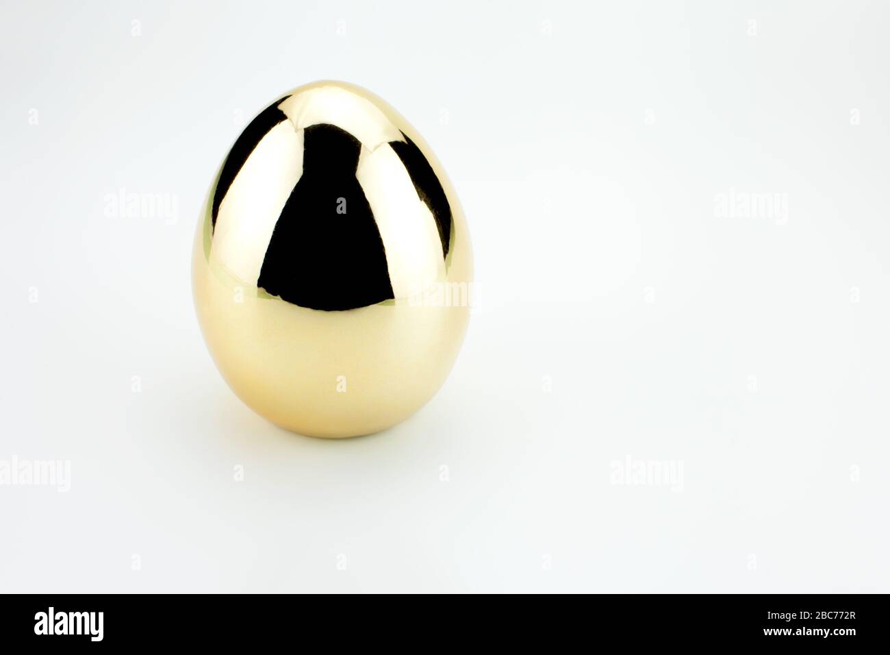 Single Shiny golden egg with reflection isolated on white Stock Photo