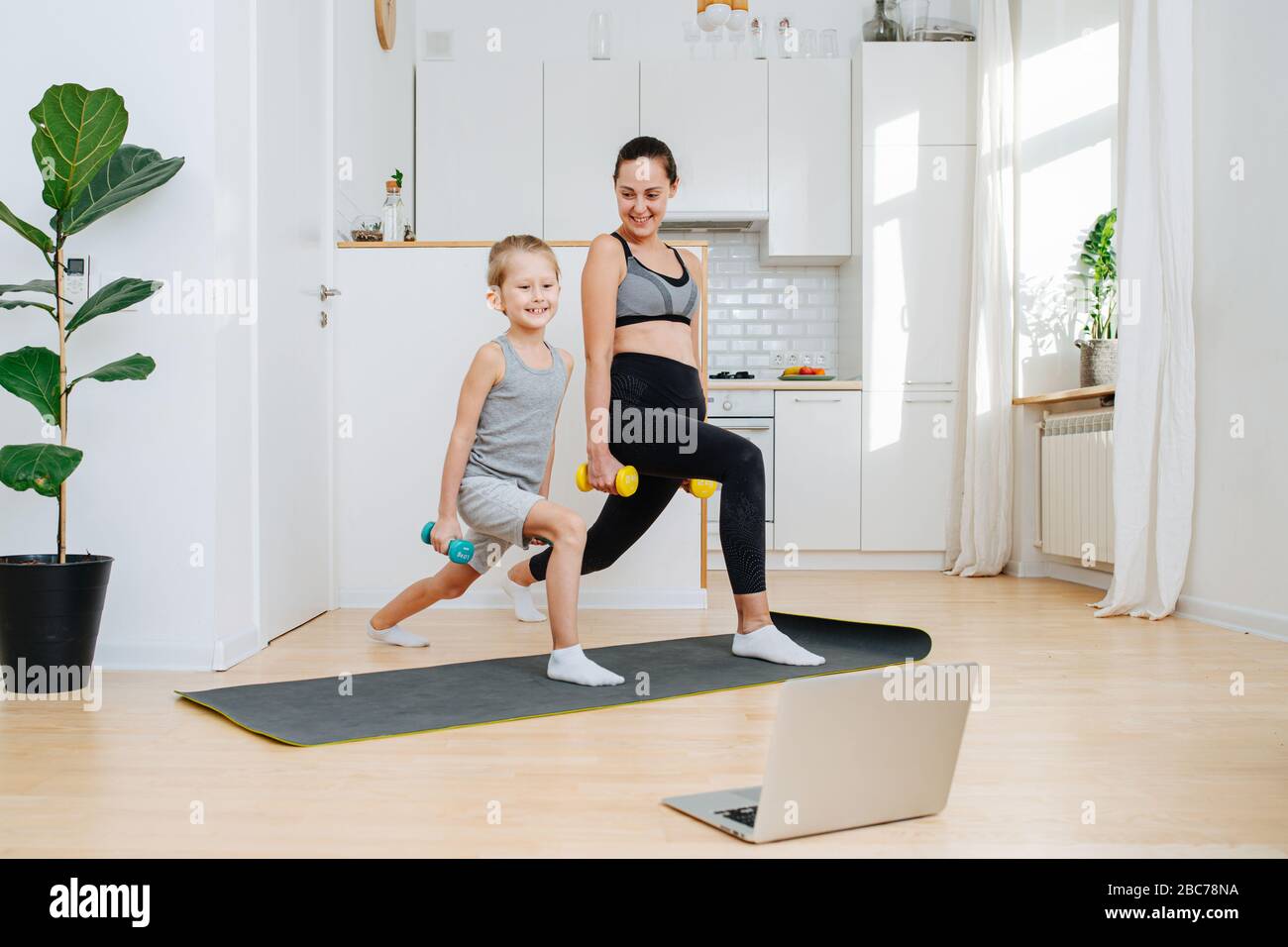 Happy mother and son exercising with dumbbells, doing forward lunges Stock Photo