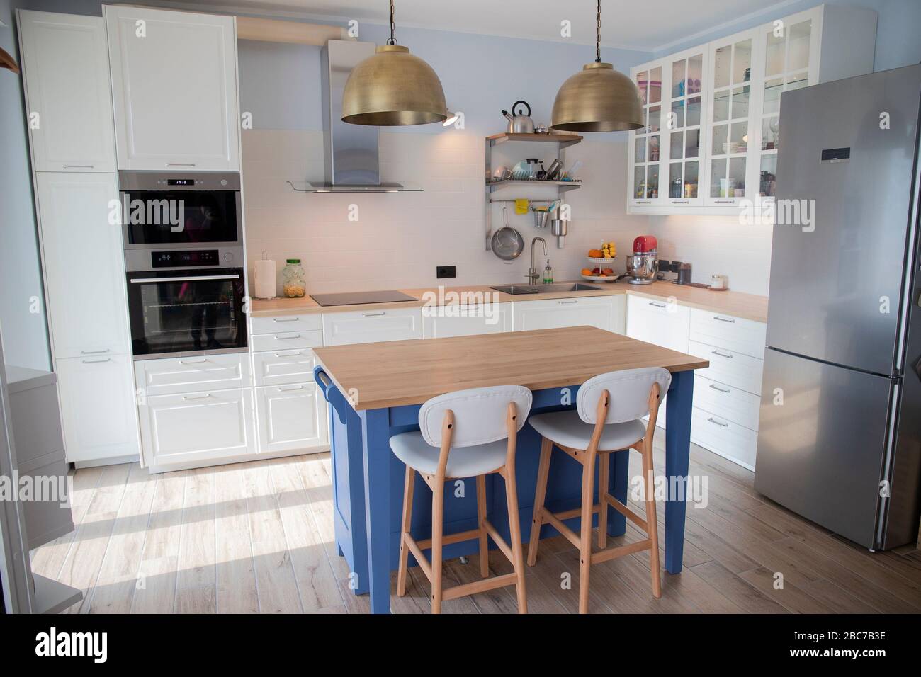White, bright kitchen with blue island and double brass pendant lights. Stock Photo