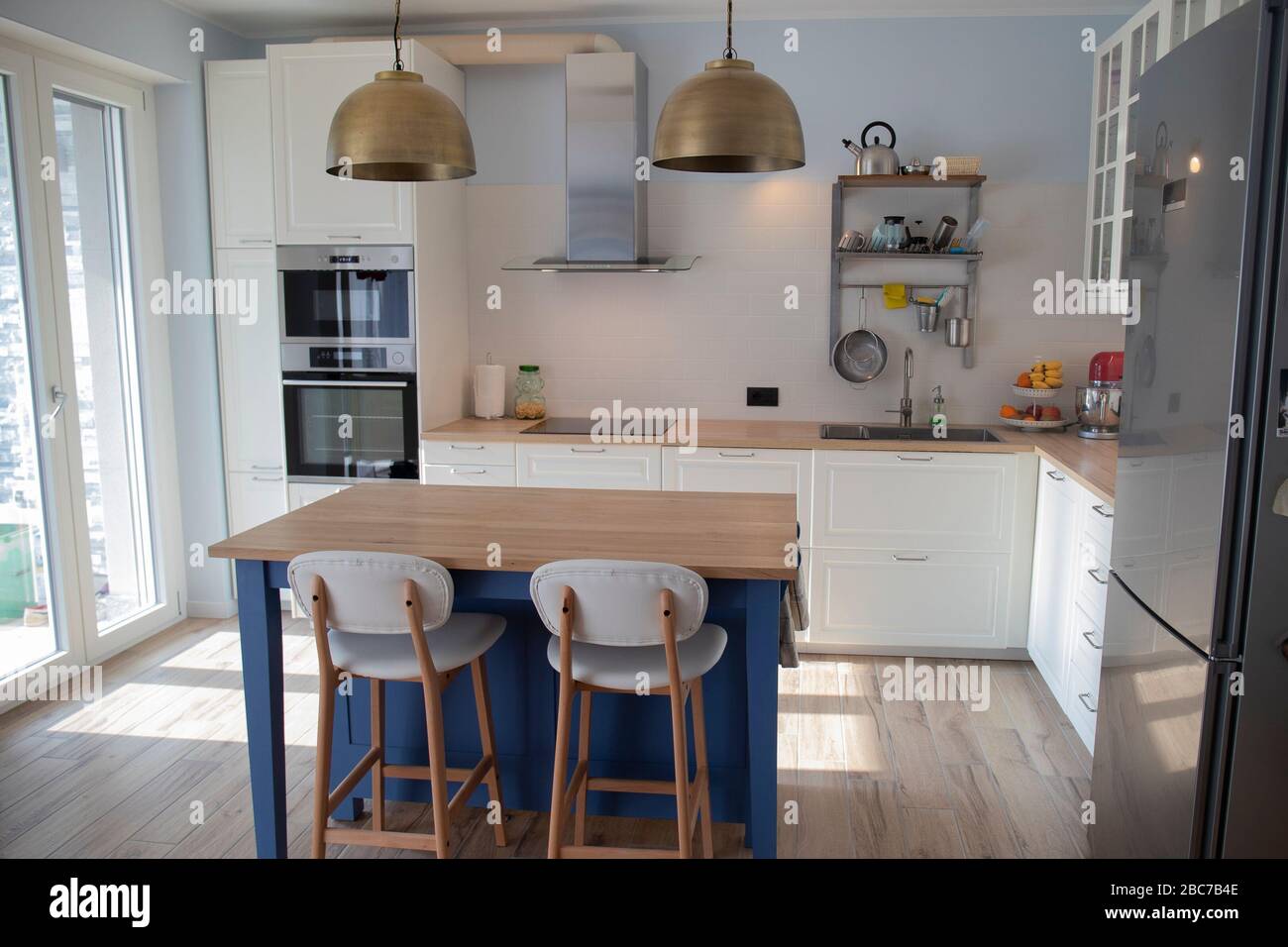 White, bright kitchen with blue island and double brass pendant lights. Stock Photo