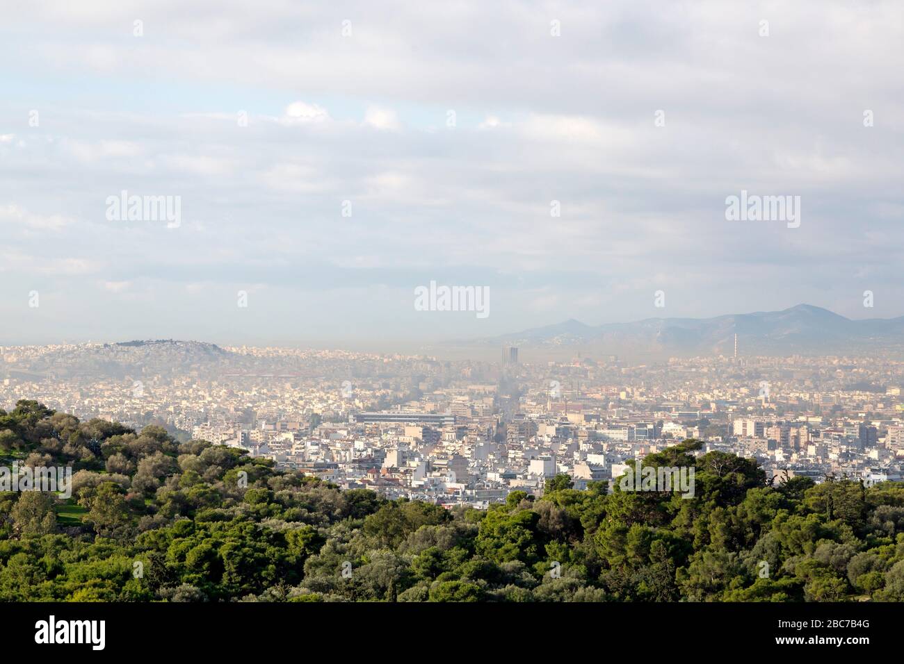 Buildings sprawl under haze in Athens, Greece. The trees of the ancient agora stand in the foreground. Stock Photo