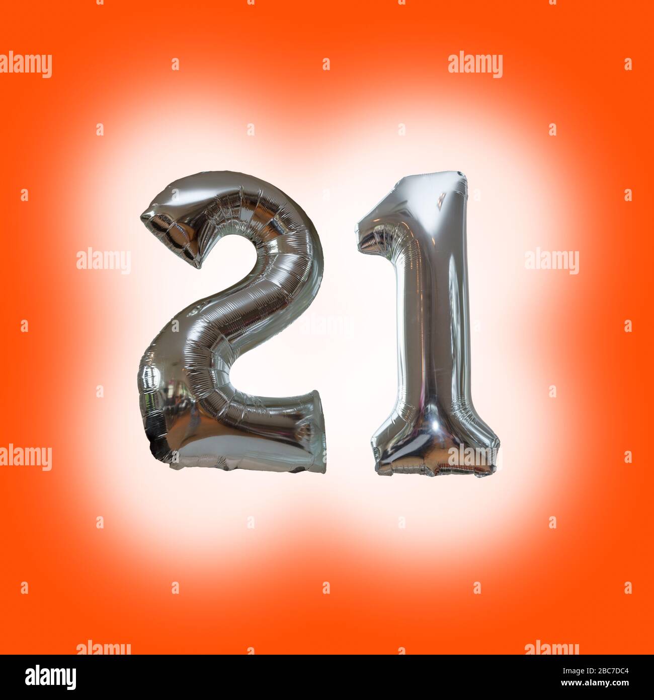 Silver number 21 party balloons isolated on a blue background  with a glow around the numbers Stock Photo