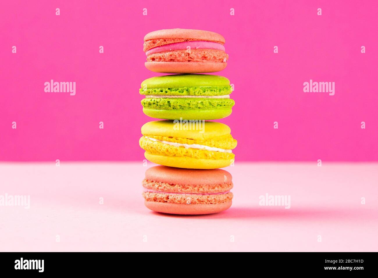 Multi-colored macaroons stand in a pile on a pink table Stock Photo