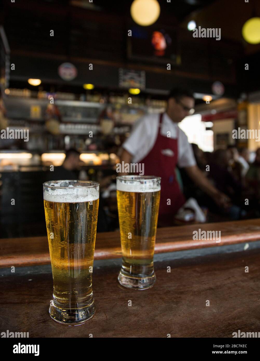 Small beers on the bar with a bar tender and people in the background Stock Photo