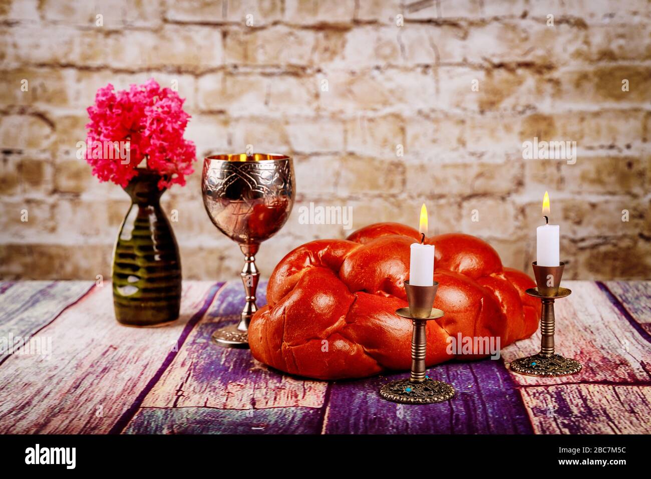 Shabbat candles in candlesticks of loaves challah for Shabbat wine in a kiddush cup with flowers Stock Photo