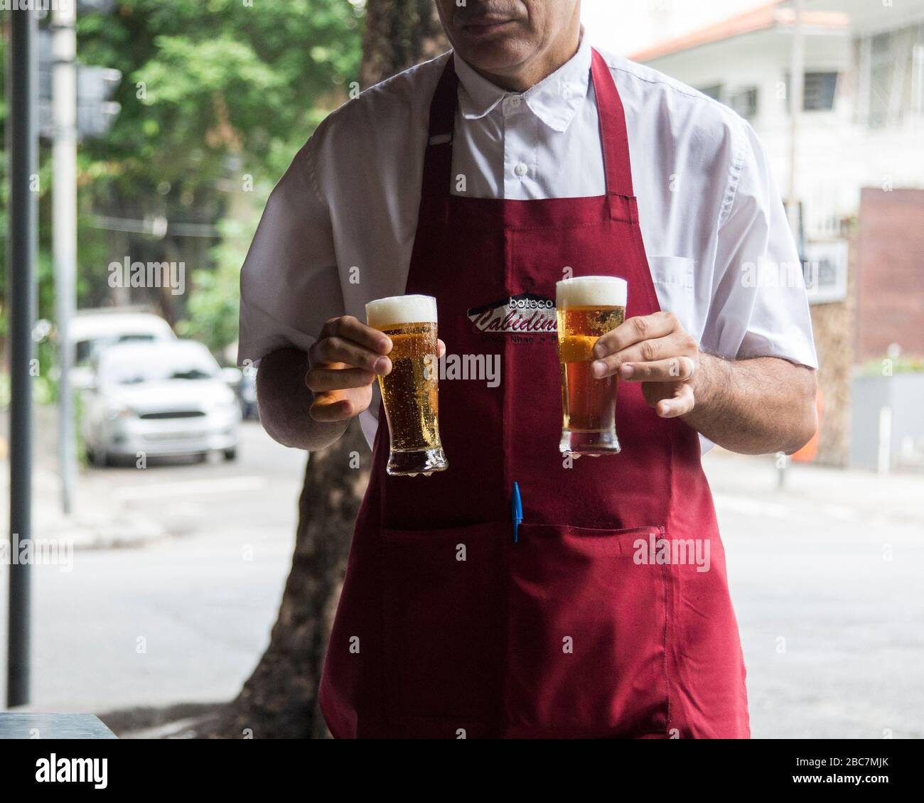 A Brazilian bar tender delivers two small beers to a table outside on the street Stock Photo