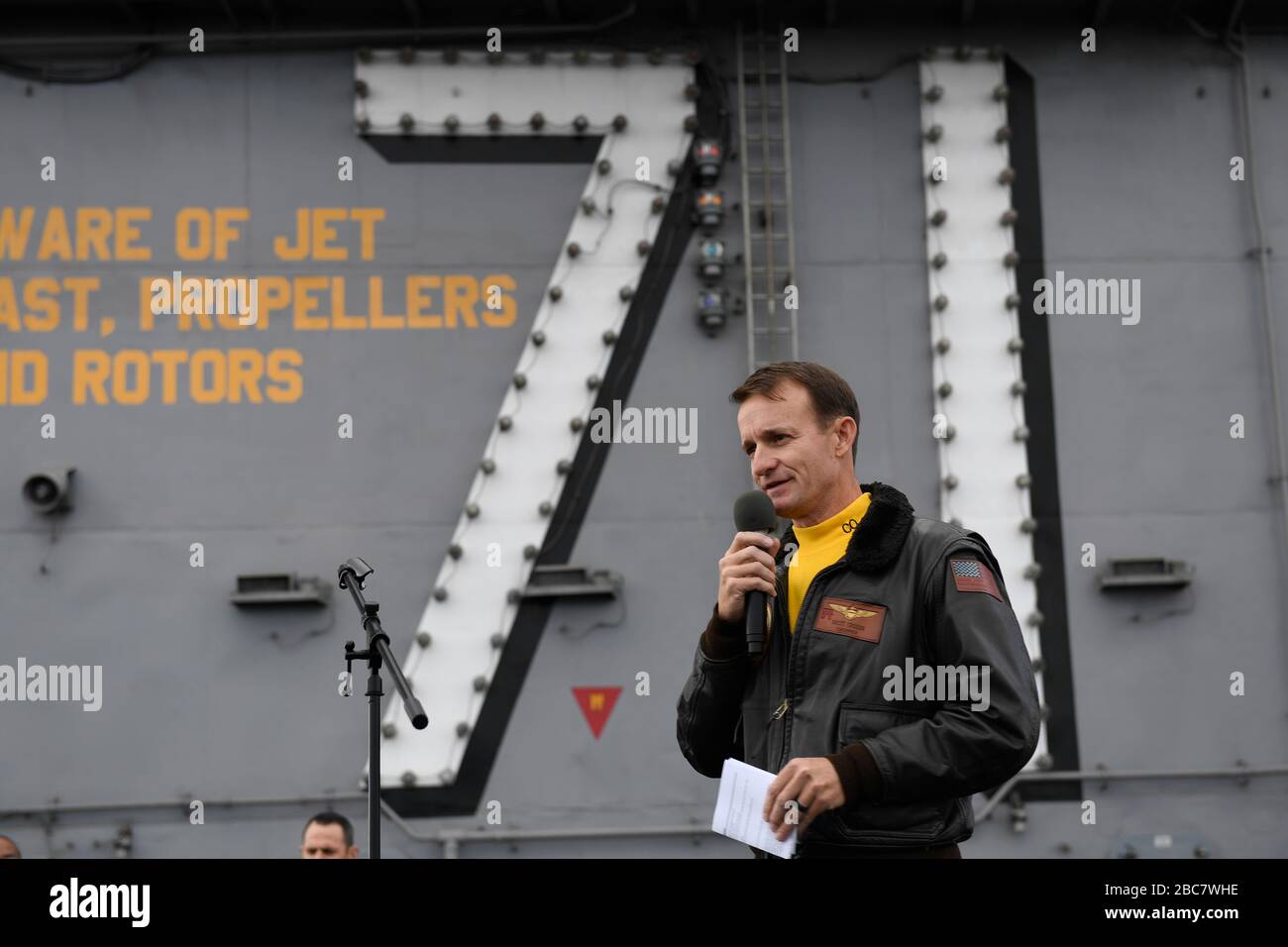 U.S. Navy Capt. Brett Crozier, commanding officer of the aircraft carrier USS Theodore Roosevelt, addresses the crew during an all-hands call on the flight deck November 15, 2019 in Eastern Pacific Ocean. Crozier was relieved of duty March 31, 2020 after writing a four-page letter to his superiors, pleading with them to take action to help stem the spread of COVID-19 cases on his ship. Stock Photo