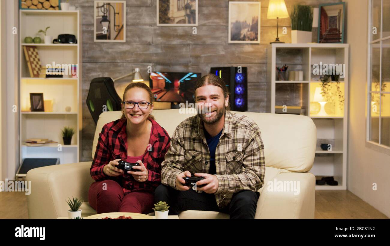Young couple jumping up from the couch celebrating their victory while playing video games using wireless controllers. Stock Photo