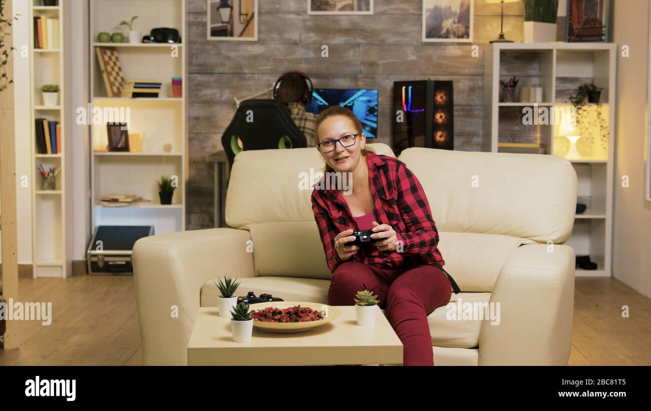 Young woman excited after her victory while playing video games in living room using wireless controller. Boyfriend in the background. Stock Photo