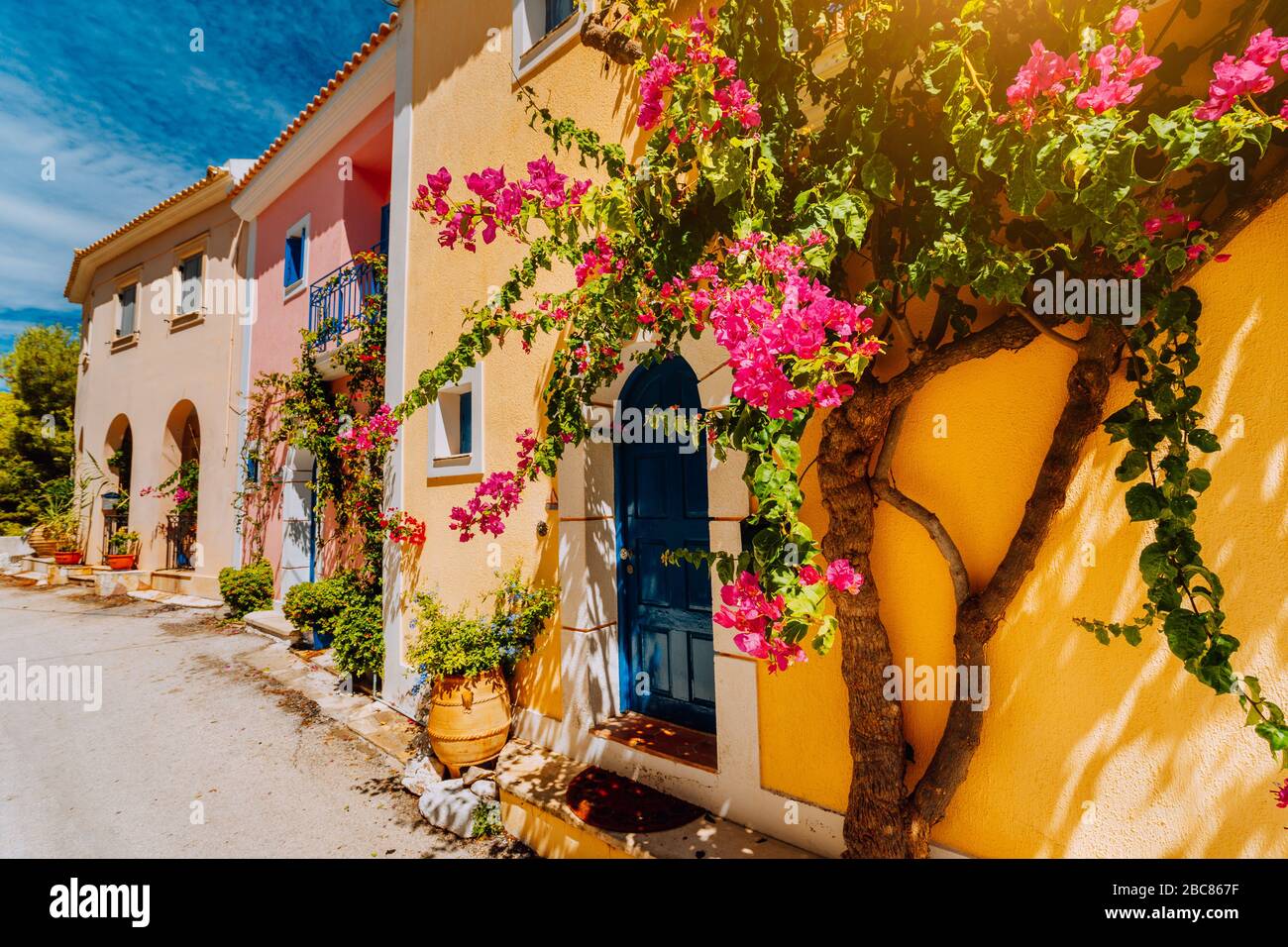 Traditional colorful greek houses in Assos village. Blooming fuchsia plant flowers growing around door. Warm sunlight. Kefalonia island, Greece. Stock Photo