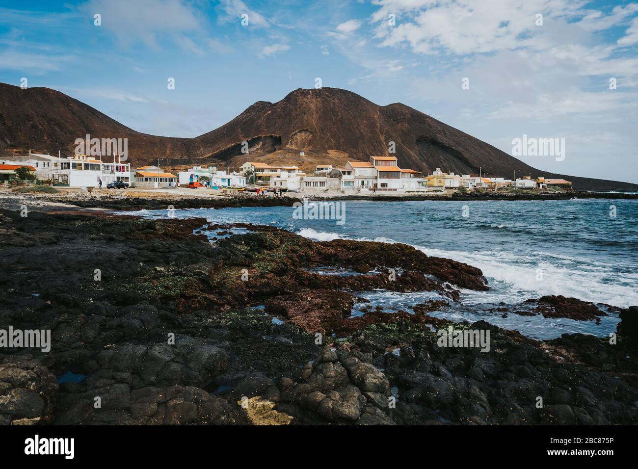 Calhau village on ocean coast in front of red colored volcanic crater. Cape Verde - Sao Vicente Island. Stock Photo