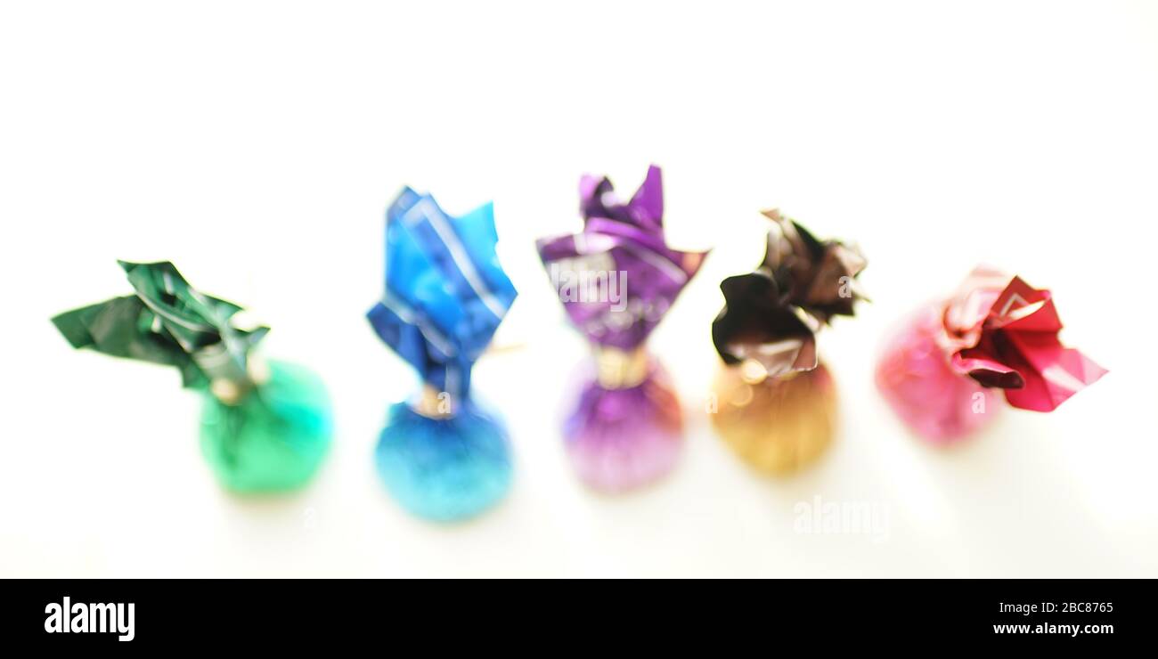 Blurred chocolate candies in colorful wrappers on white table, selective focus. Stock Photo
