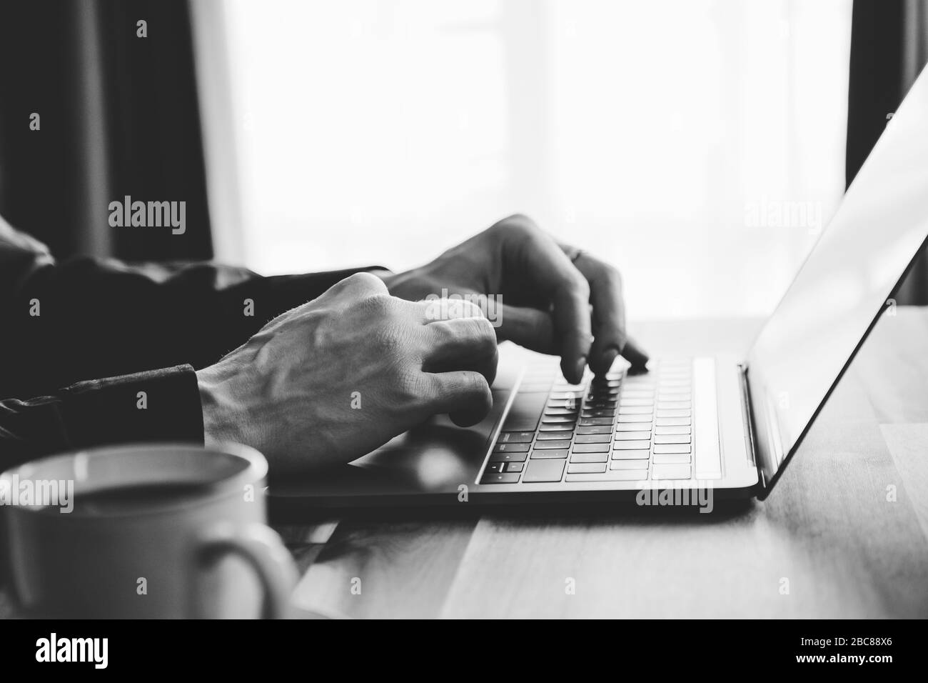 A man is typing on a laptop keyboard. Concept of work from home, black and white photo. Stock Photo