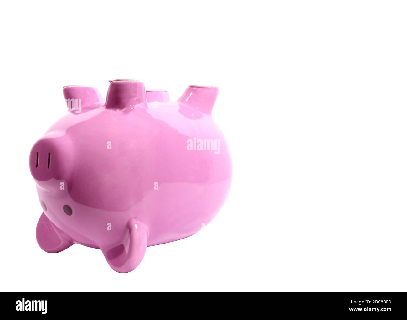 Horizontal side view shot of a pink piggy bank on its back on the left side of the picture.  White background with lots of copy space. Stock Photo